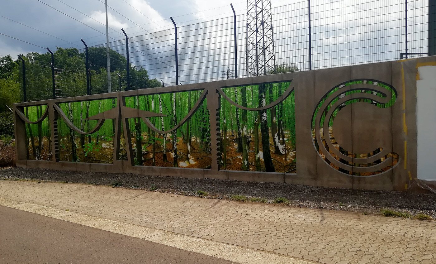 Stützwand am Umspannwerk: gemalter Birkenwald hinter gemalten Beton-Ornamenten