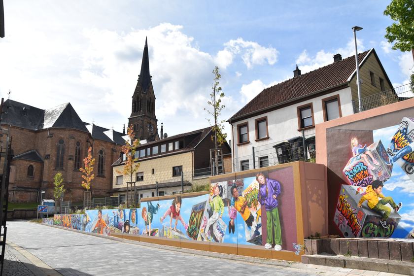 Gesamtansicht der bemalten Stützmauer mit Kirche im Hintergrund