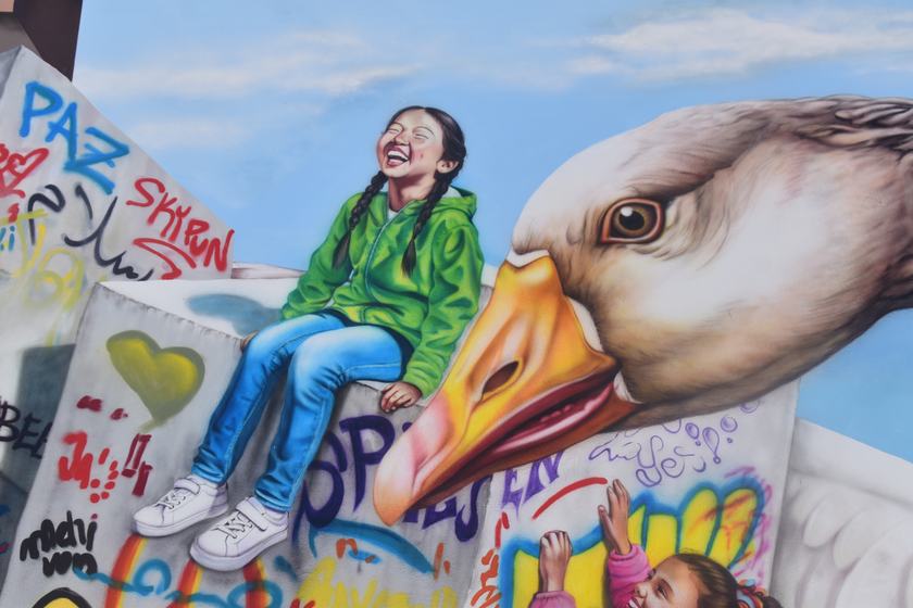 Mädchen in grüner Jacke auf einem Quader neben der Gans